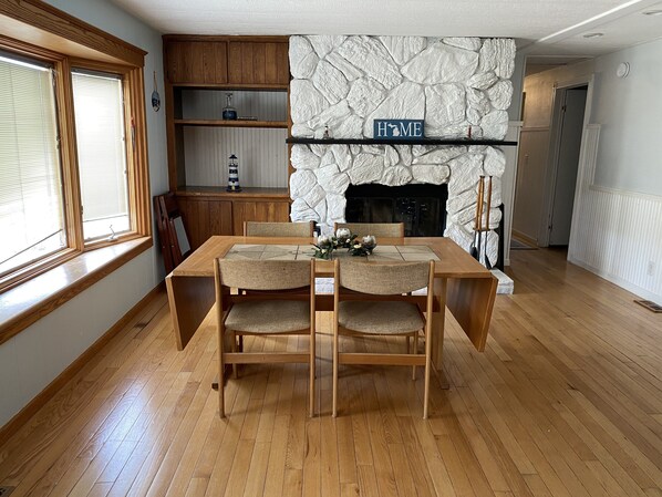 Un comedor con mesa y sillas de madera, chimenea de piedra y estanterías de madera.