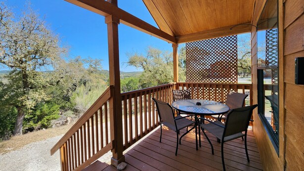A wooden deck with a table and chairs, overlooking a scenic landscape with trees and hills. - Cozy Canyon Lake Tiny House – Stunning Views & Great Location (Canyon Lake)