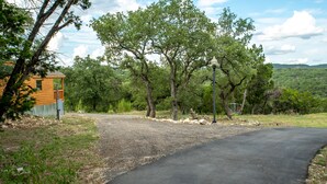 A gravel driveway leading to a wooden cabin with a metal fence, surrounded by trees and a metal lamp post. - Cozy Canyon Lake Tiny House – Stunning Views & Great Location (Canyon Lake)