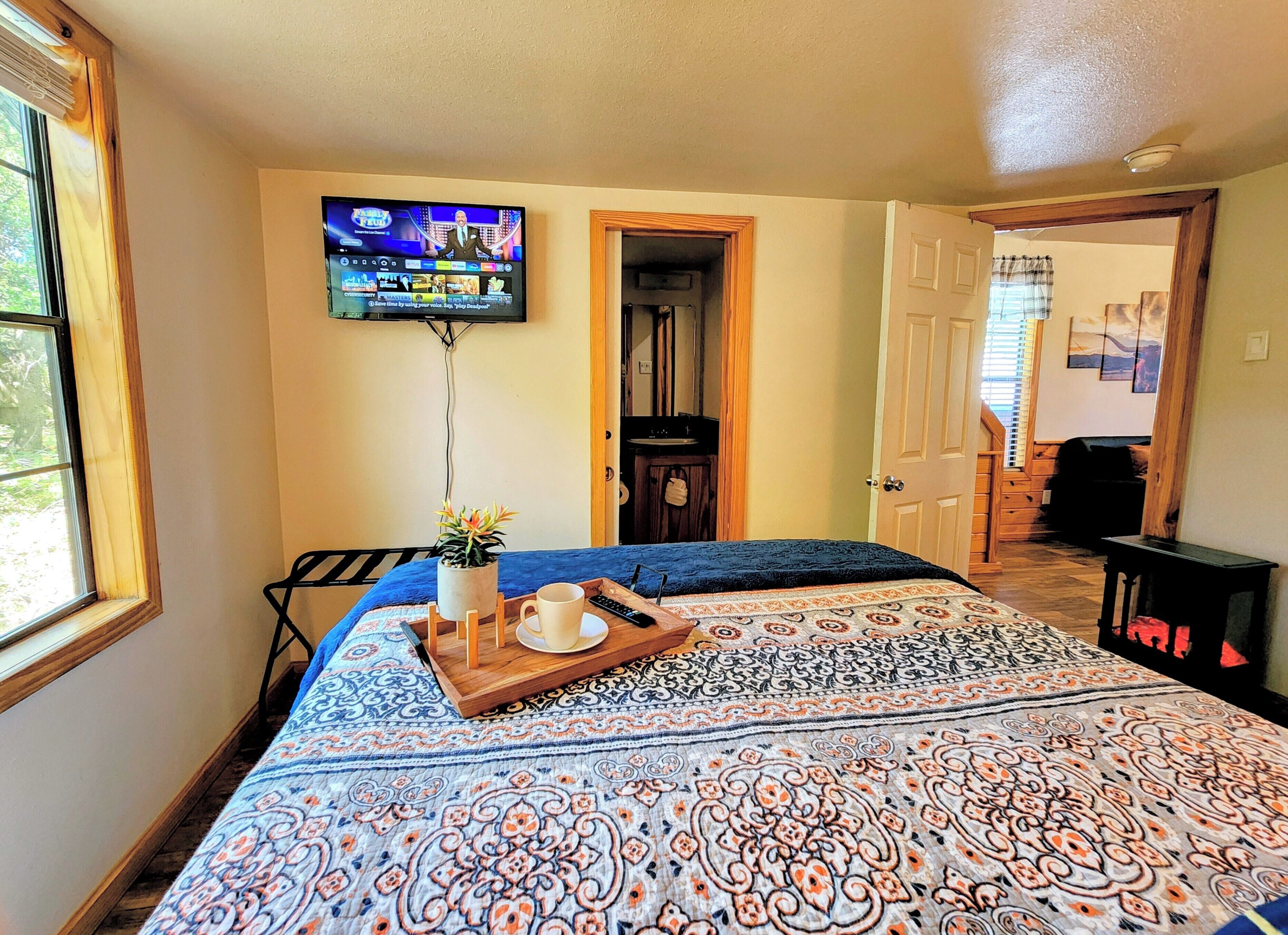 A bedroom with a large bed, a television mounted on the wall, a wooden door, and a window.
