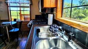 A compact kitchen with a stove, sink, and window overlooking a green landscape. - Cozy Canyon Lake Tiny House – Stunning Views & Great Location (Canyon Lake)