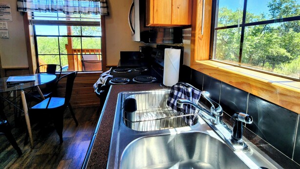 A compact kitchen with a stove, sink, and window overlooking a green landscape. - Cozy Canyon Lake Tiny House – Stunning Views & Great Location (Canyon Lake)