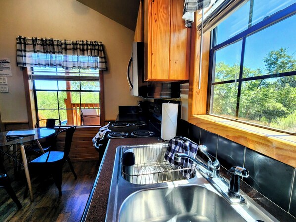 A compact kitchen with a stove, sink, and window overlooking a green landscape. - Cozy Canyon Lake Tiny House – Stunning Views & Great Location (Canyon Lake)
