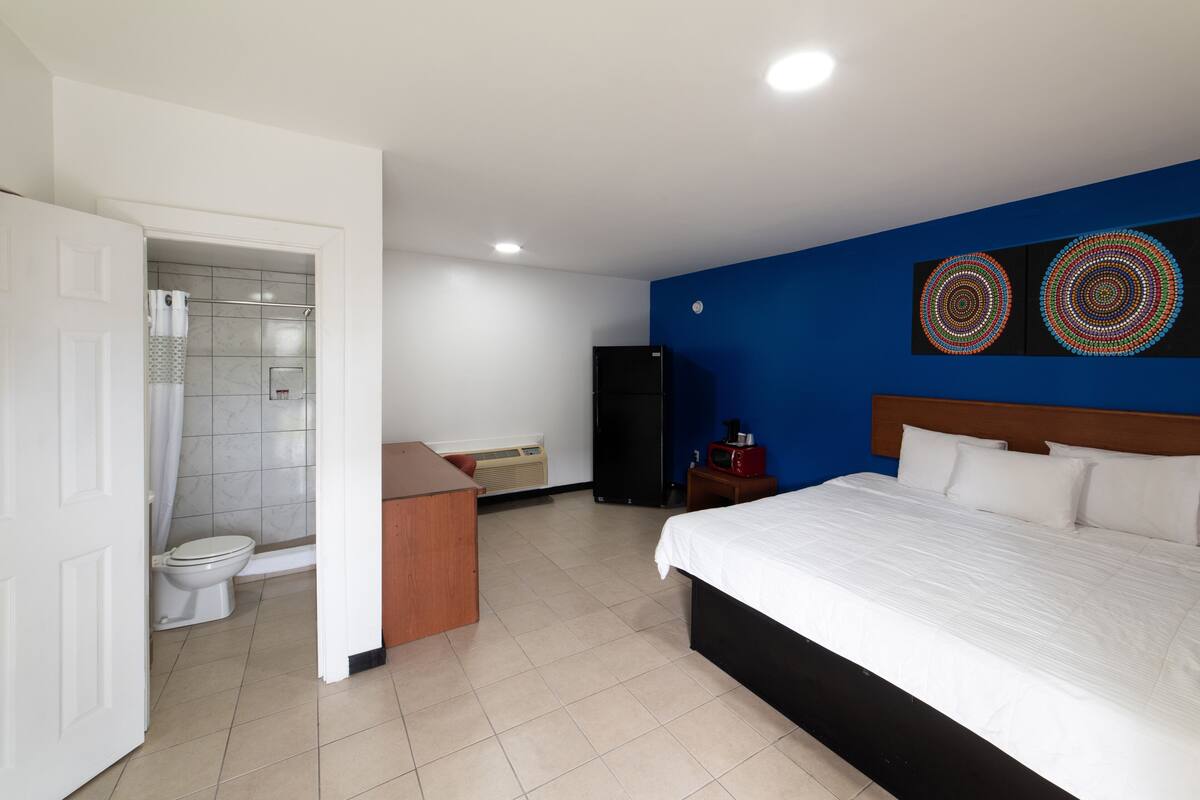 Ein Hotelzimmer mit Bett, Badezimmer mit Toilette und Dusche, einem Holztisch und zwei Wandbildern.
