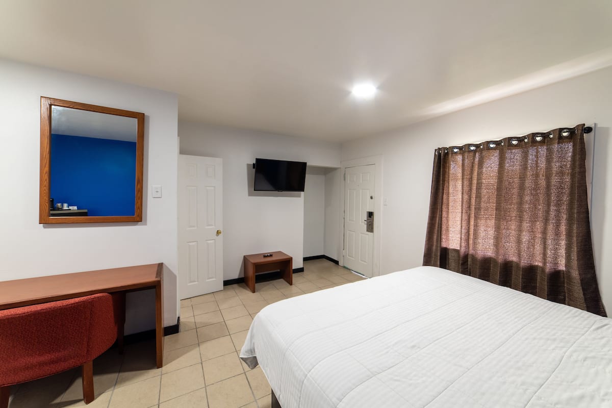 Ein Hotelzimmer mit einem Bett, einem Schreibtisch, einem Stuhl, einem Fernseher und einer Tür.