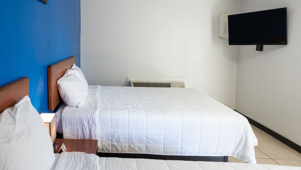 A hotel room with a bed, a flat-screen TV mounted on the wall, and a window with blue walls. - American Inn (Baton Rouge)