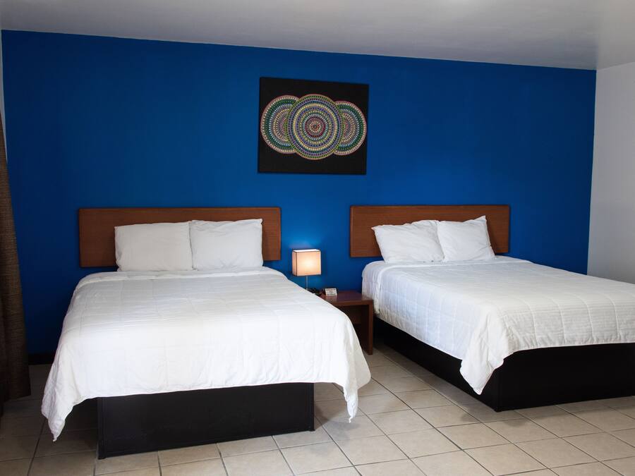 A hotel room with two beds, a blue accent wall, and a decorative art piece above the beds.