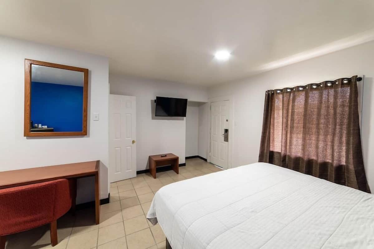 Ein Hotelzimmer mit Bett, Schreibtisch, Stuhl, Fernseher und Vorhang.