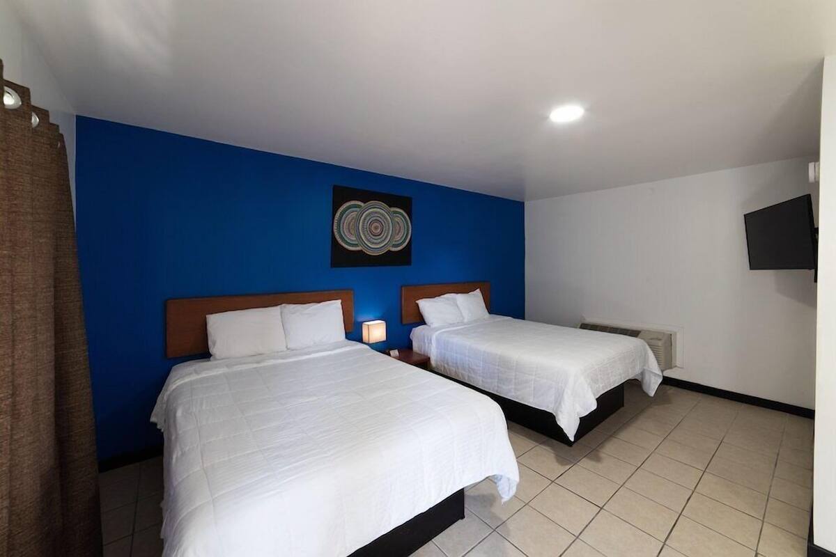 Ein Hotelzimmer mit zwei Betten, einer blauen Akzentwand, einem Flachbildfernseher und einer Deckenleuchte.