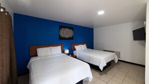 A hotel room with two beds, a blue accent wall, a decorative wall piece, and a flat-screen TV. - American Inn (Baton Rouge)