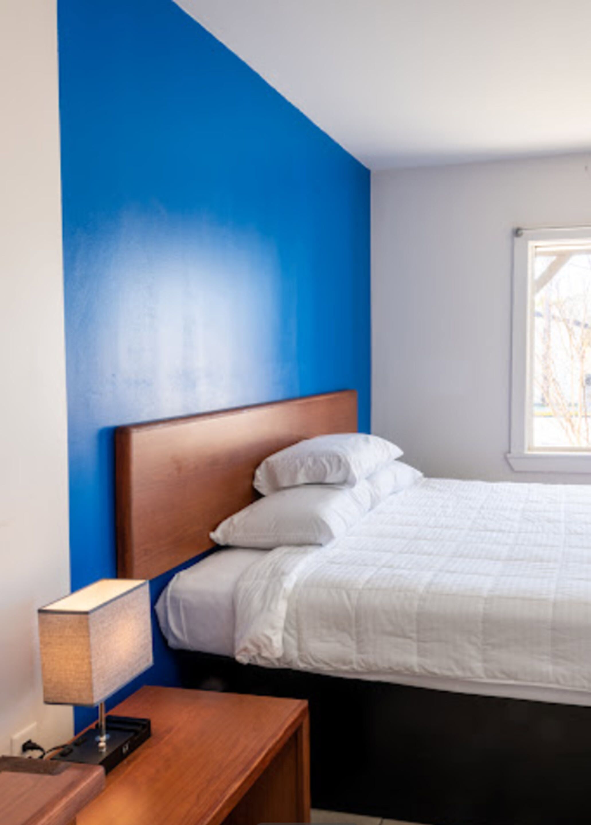 A bedroom with a wooden headboard, white bedding, and a bedside table with a lamp.