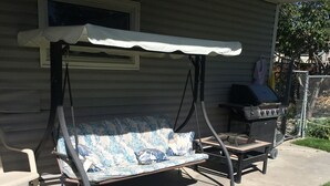 A patio with a swing seat, a grill, and a concrete walkway.