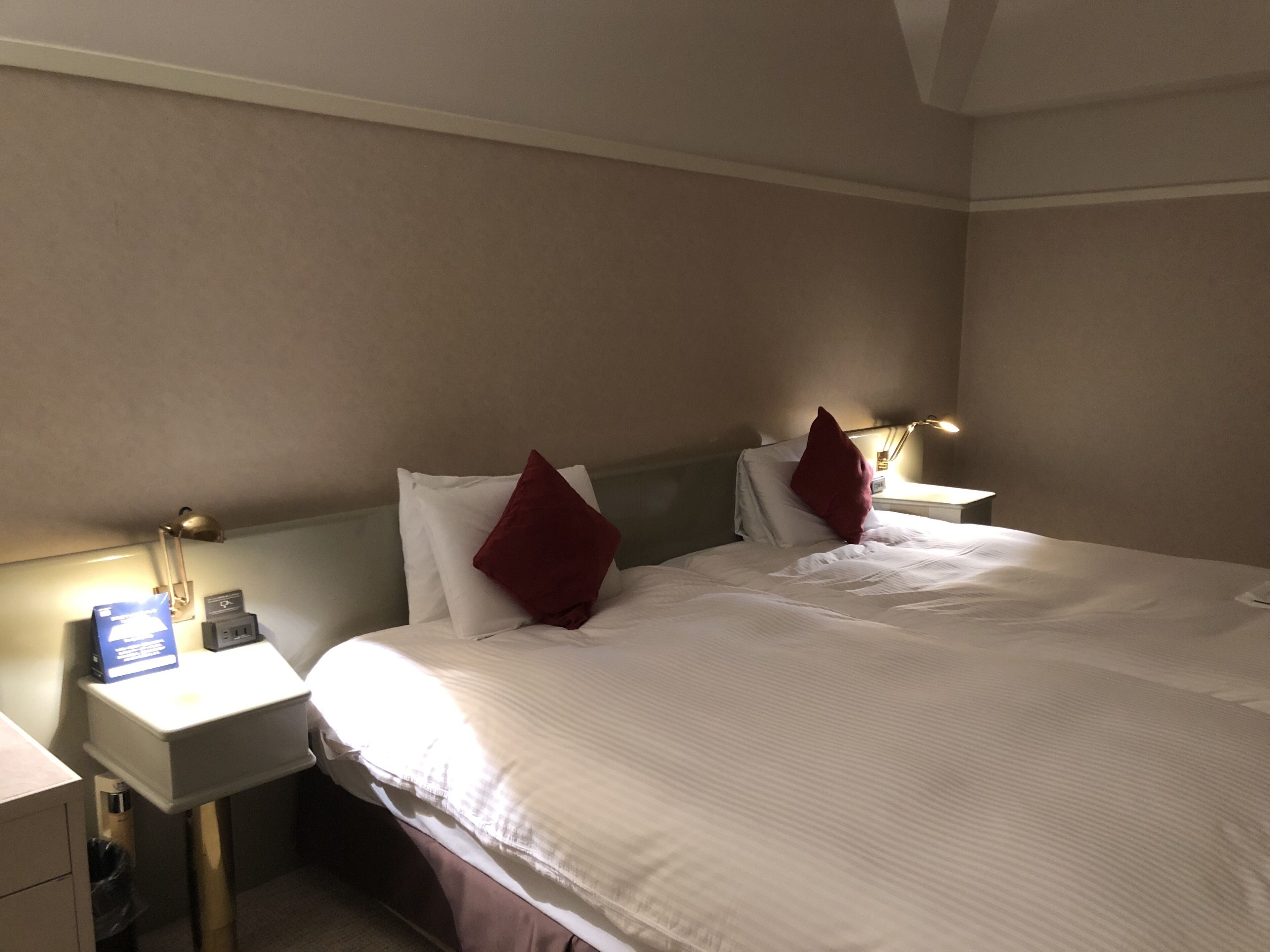 A hotel room with a bed, two bedside tables, a nightstand, a lamp, and a wall-mounted light.