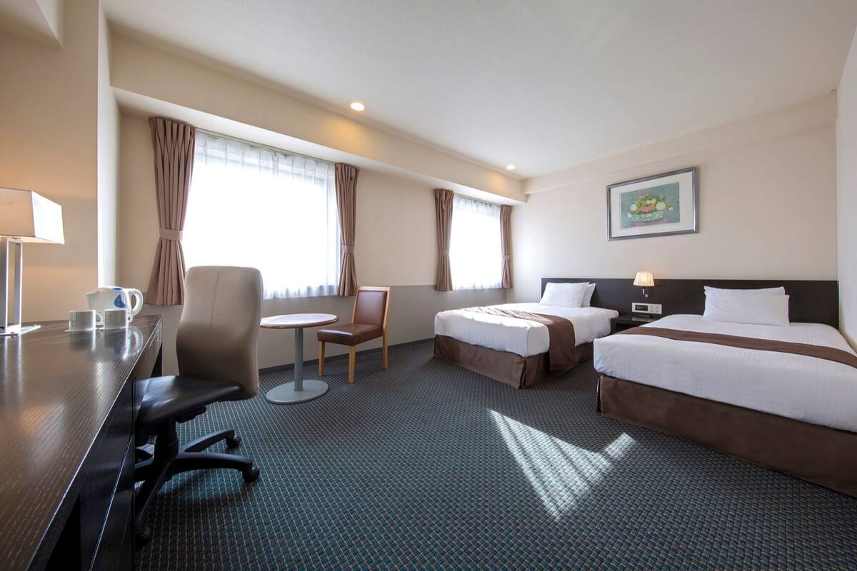 A hotel room with a bed, a desk, a chair, and a small table.