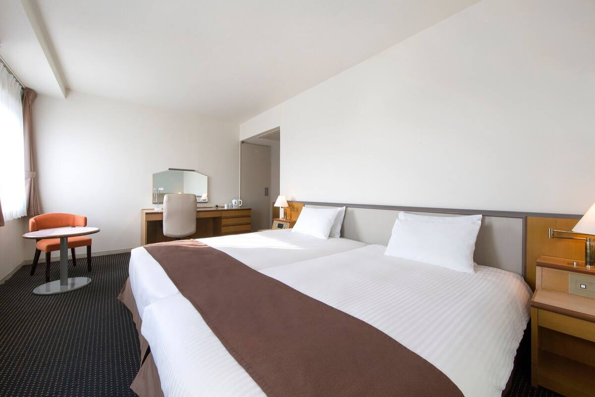 A hotel room with a large bed, a desk with a chair, a small table, and a mirror.