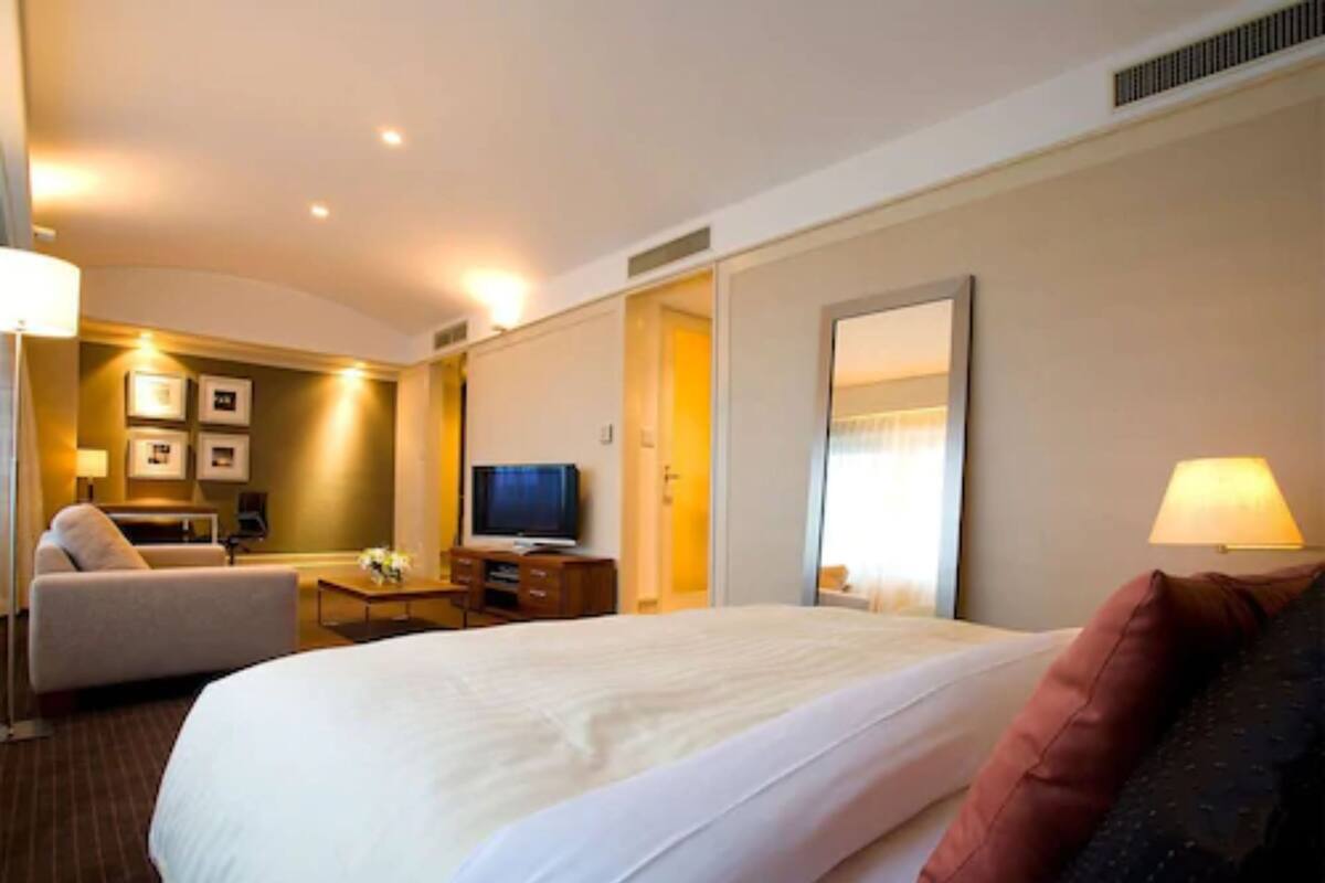 A hotel room with a large bed, a television, a desk with a lamp, and a sofa.