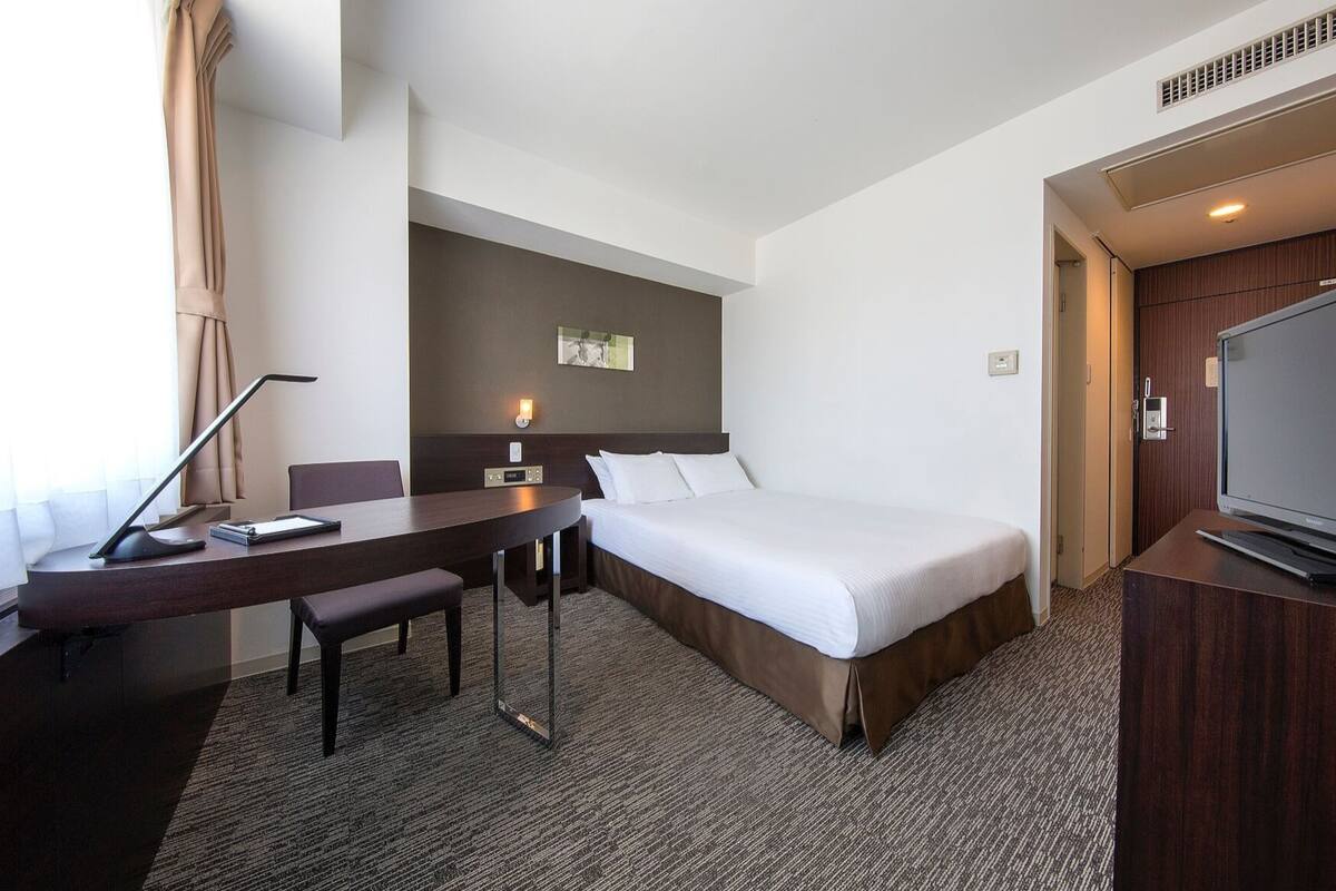 A hotel room with a bed, desk, chair, TV, and a picture on the wall.