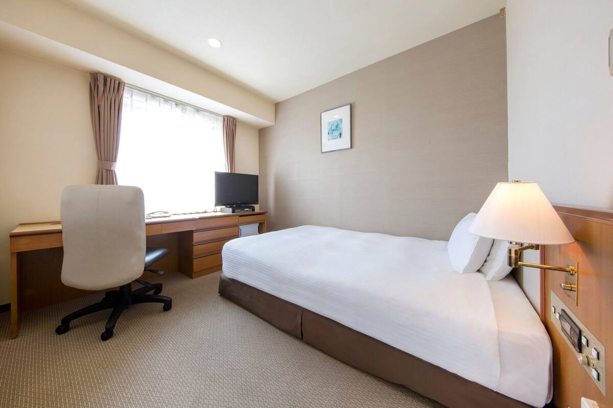 A hotel room with a bed, desk, chair, television, and a lamp.