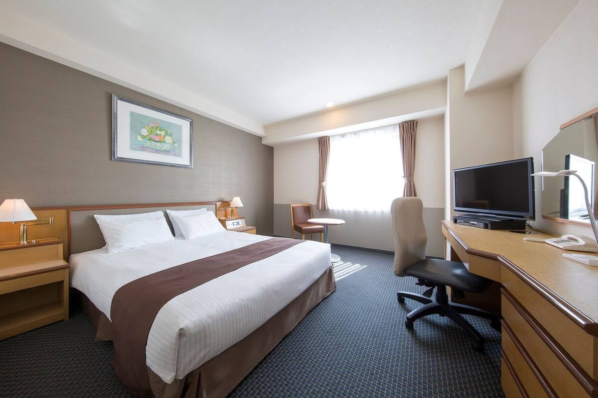 A hotel room with a large bed, a desk with a computer, a chair, a TV, and a small table.