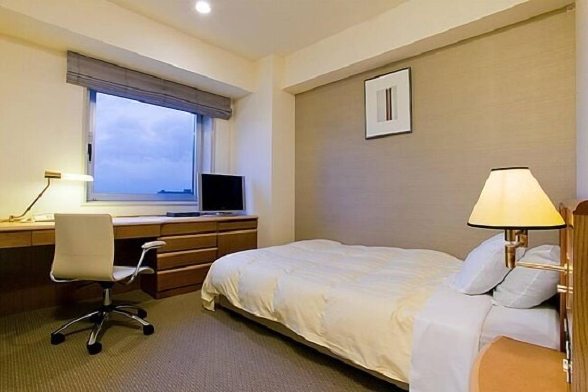 A hotel room with a bed, desk, chair, and a window with a view.