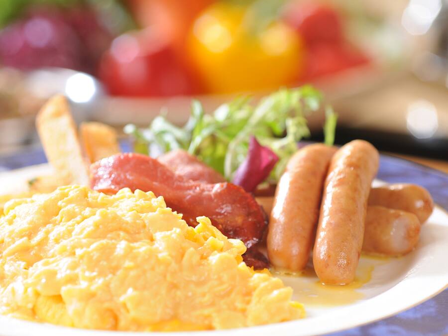 A plate with scrambled eggs, sausages, and bacon.