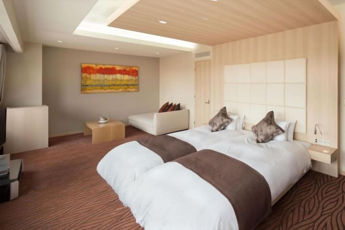 A hotel room with two beds, a sofa, a TV, and a painting on the wall.