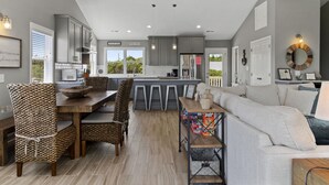 Een moderne keuken met grijze kastjes, een eethoek met rieten stoelen en een grijze bank.