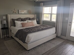 A bedroom with a bed, a nightstand, a lamp, and a window with curtains. - OCEAN VIEW, across from beach access, BEAUTIFULLY updated 4 bed,4 bath,sleeps 14 (Emerald Isle)