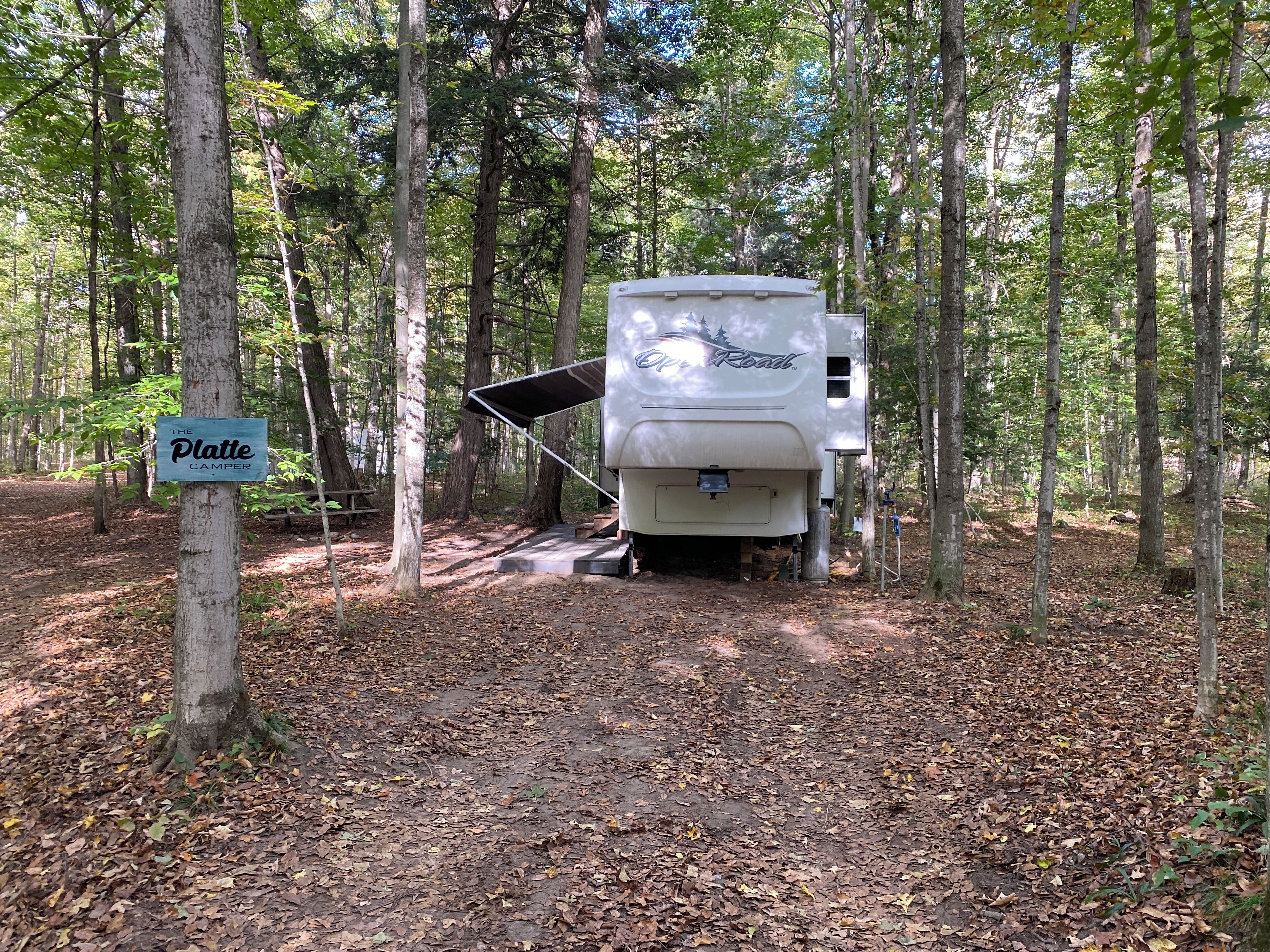 A white RV with a black awning parked in a wooded area.