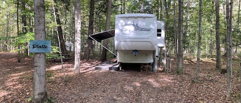 A white RV with a black awning parked in a wooded area.