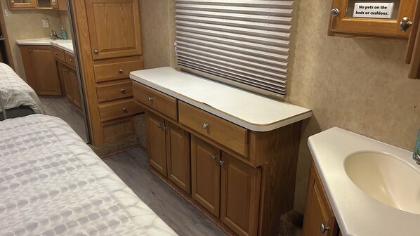 Une petite salle de bain pour camping-car, dotée de meubles en bois, d’un lavabo et d’une fenêtre avec stores.