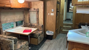 A compact RV interior with a dining table, seating area, and kitchenette. - Platte - 37ft RV Camper in the Woods with Fire pit &  Hot Tub Access (Benzonia)