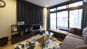 Un salon moderne avec un canapé, un téléviseur, une table basse et une grande fenêtre avec des rideaux.