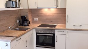 A compact kitchen with white cabinets, a built-in oven, and a coffee maker. - Huus Windroos (Jemgum)