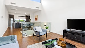 A spacious living area with a modern kitchen, a glass staircase, and a large TV. - Little Grenfell Apartments by Urban Rest (Kent Town)