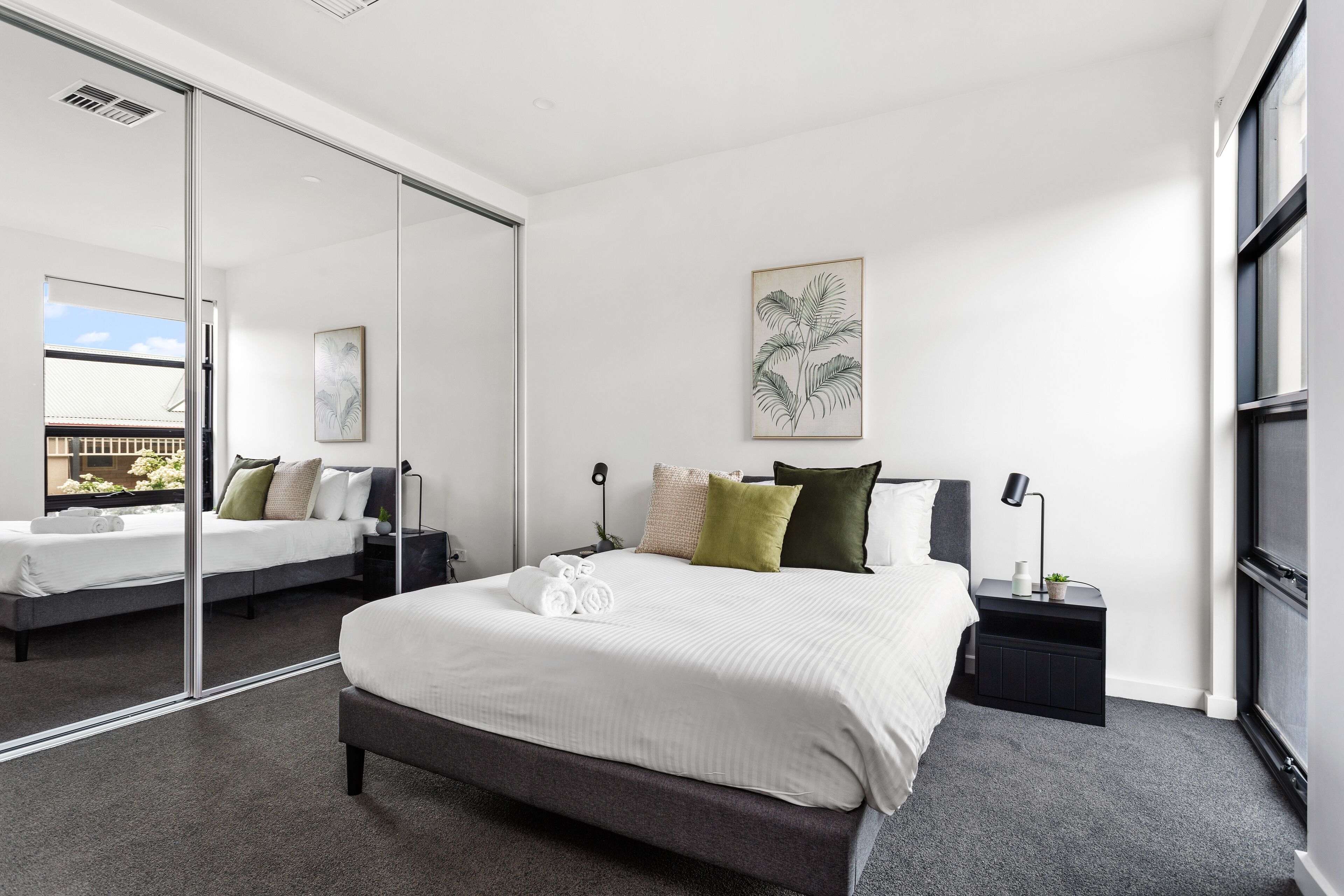 Un dormitorio moderno con una cama grande, una mesita de noche con lámpara y un espejo amplio.