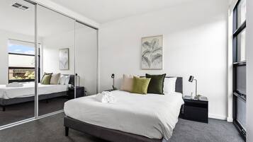Un dormitorio moderno con una cama grande, una mesita de noche con lámpara y un espejo amplio.