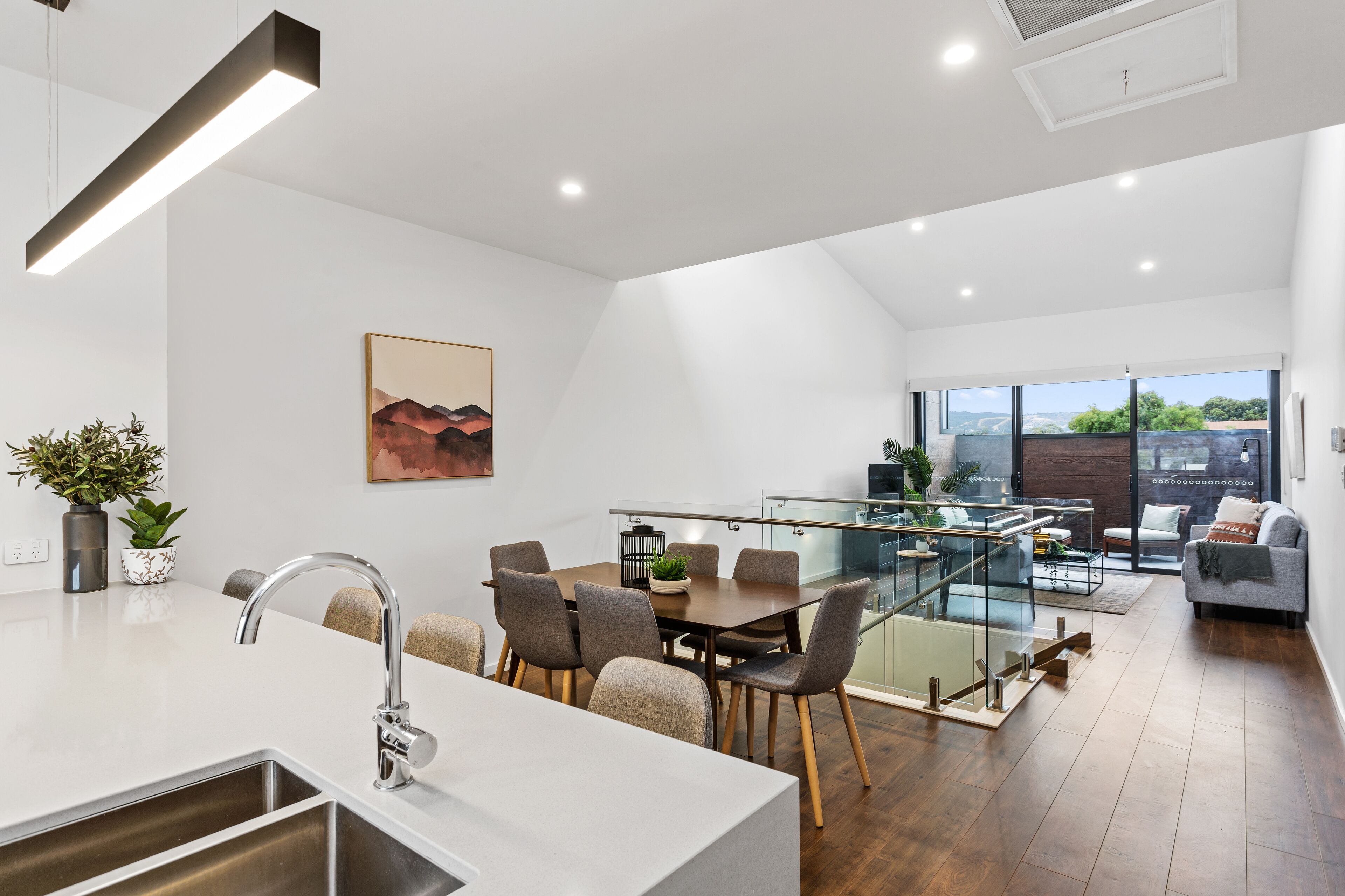 A modern kitchen with a dining area, a staircase leading to a balcony, and a living area with a sofa.