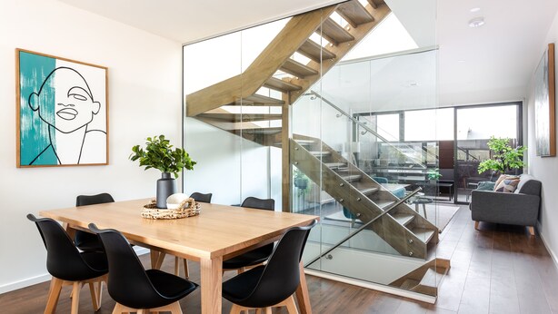 A modern interior with a wooden dining table, black chairs, a glass staircase, and a living area with a sofa and plants. - Little Grenfell Apartments by Urban Rest (Kent Town)