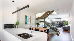A modern kitchen with a large island, a dining area with a glass staircase, and a living room with a sofa and a plant. - Little Grenfell Apartments by Urban Rest (Kent Town)