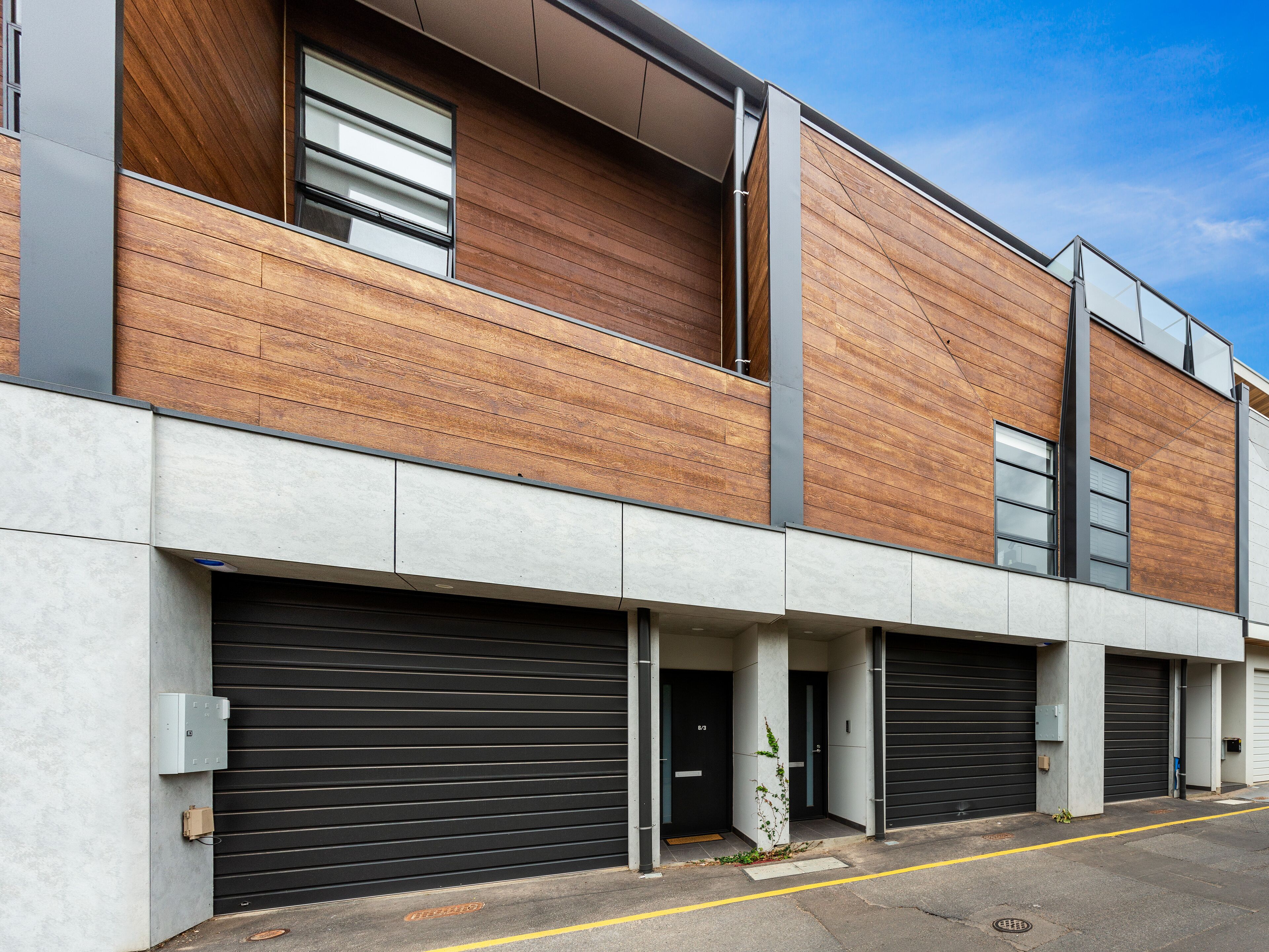 A modern building with a wooden facade, large garage doors, and a clear sky.