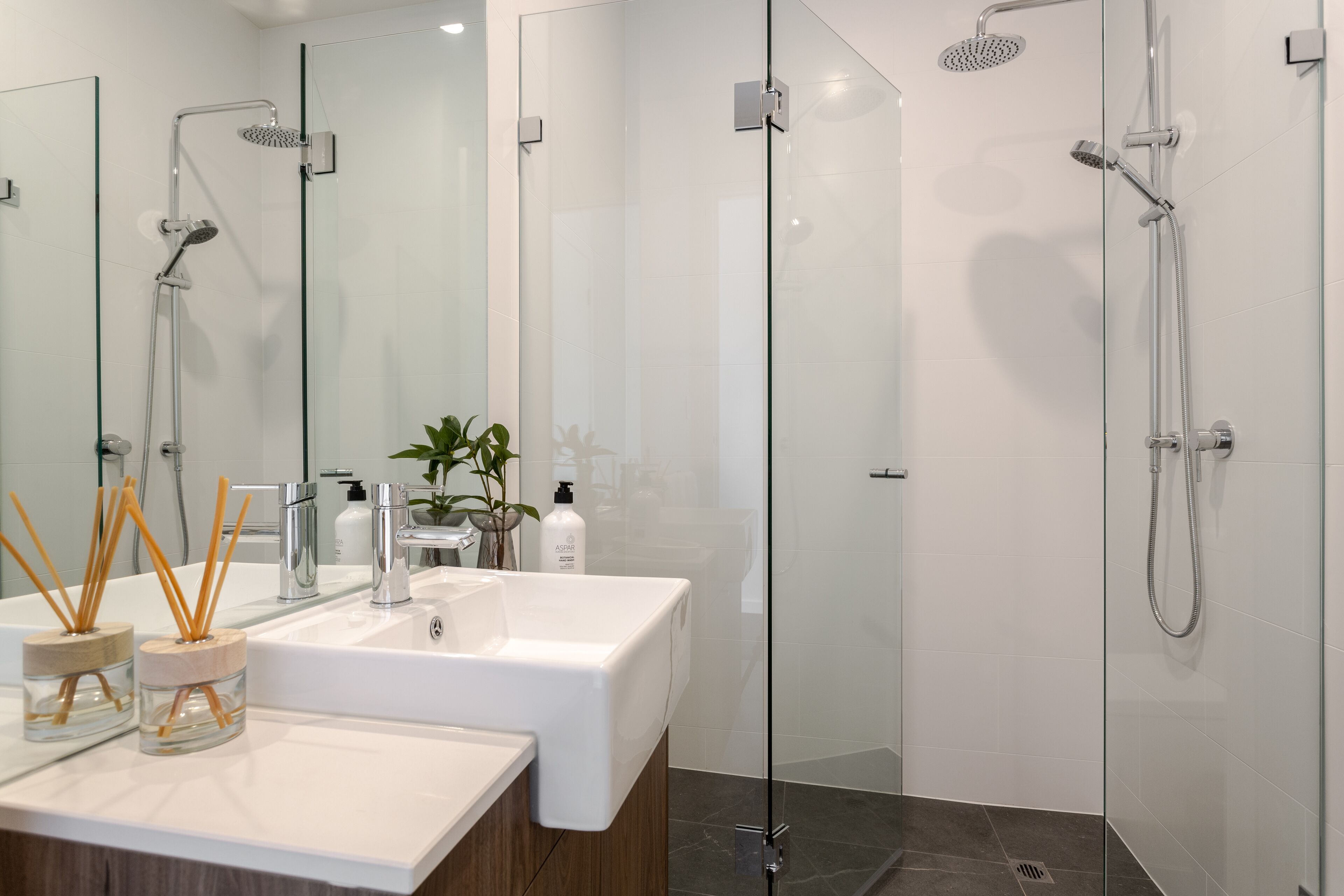 A modern bathroom with a glass shower enclosure, a white sink, and a mirror.