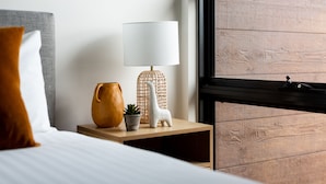 A neatly arranged hotel room with a bed, a bedside table with a lamp, a small potted plant, and a decorative item resembling a llama. - Little Grenfell Apartments by Urban Rest (Kent Town)