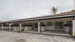 Ein zweistöckiges Motel mit überdachtem Außenbereich, einer Palme und einem geparkten Auto.