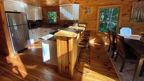 Interior de cabana com cozinha, área de jantar e banquetas de bar.