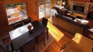 Uma cabana com área de jantar, sofá, lareira e várias janelas.