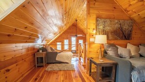 Um quarto de sótão acolhedor com paredes de madeira, um sofá, uma mesa e um abajur.