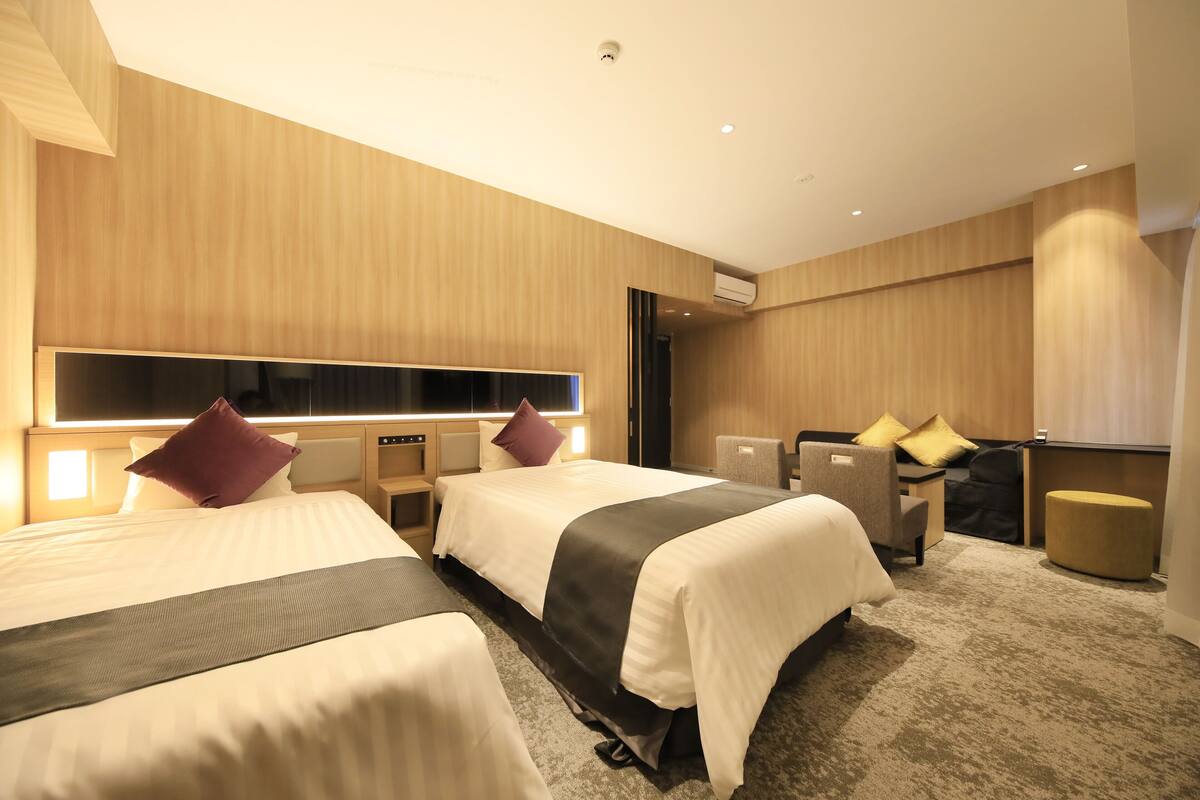 A hotel room with two beds, a desk, a chair, and a sofa.