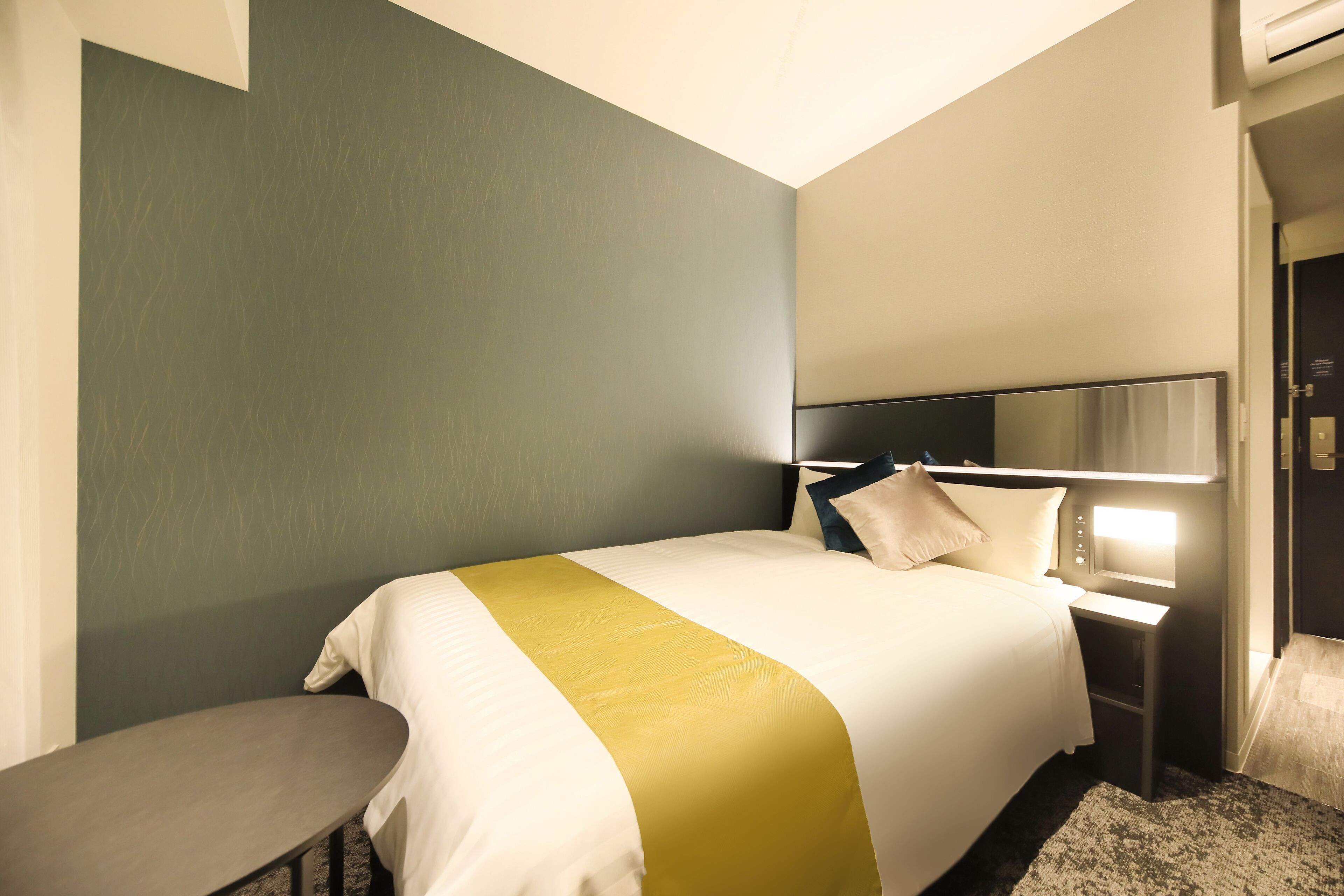 A hotel room with a bed, bedside table, and a bench.