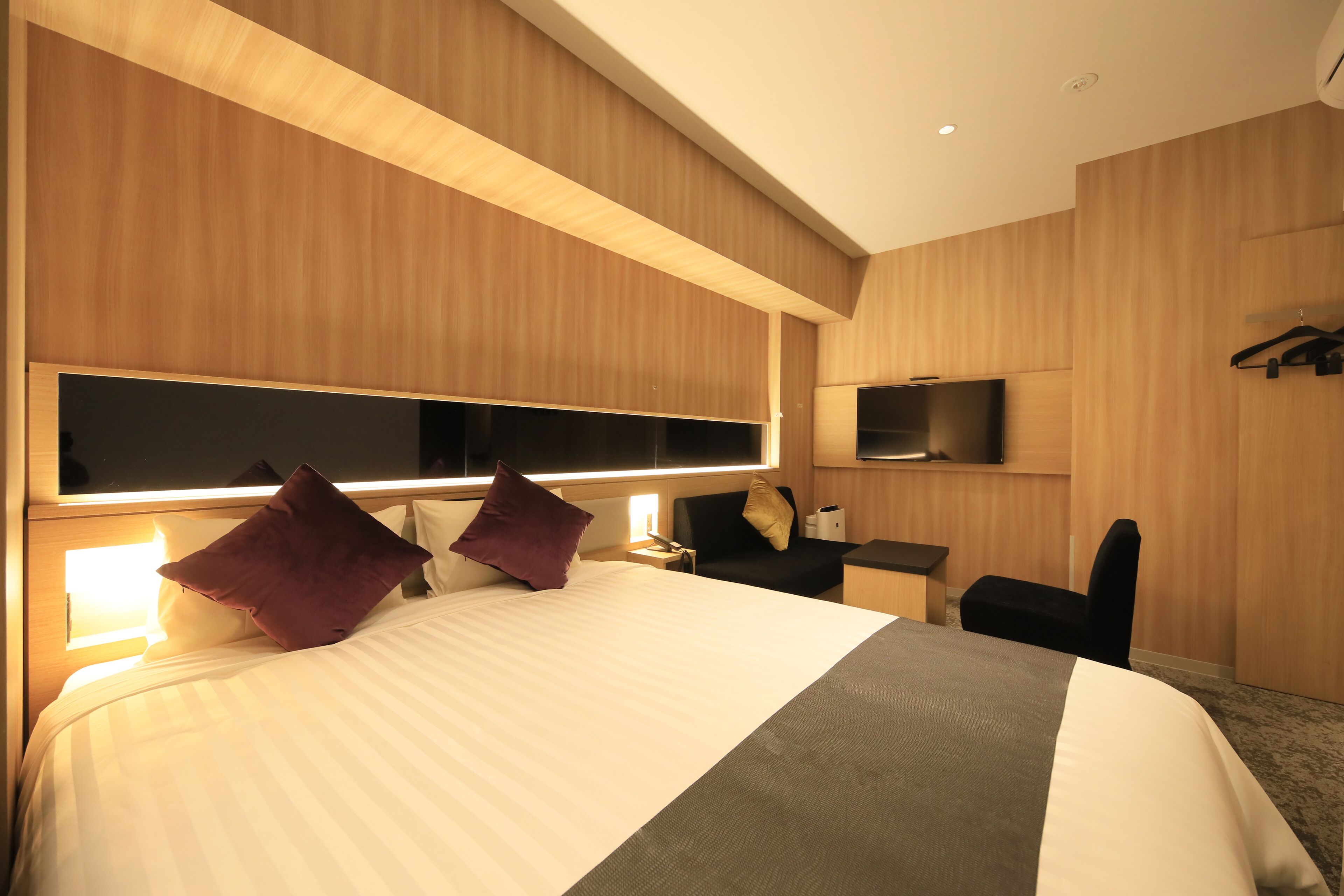 Una habitación de hotel moderna con una cama grande, lámparas de noche, un escritorio y un televisor de pantalla plana montado en la pared.